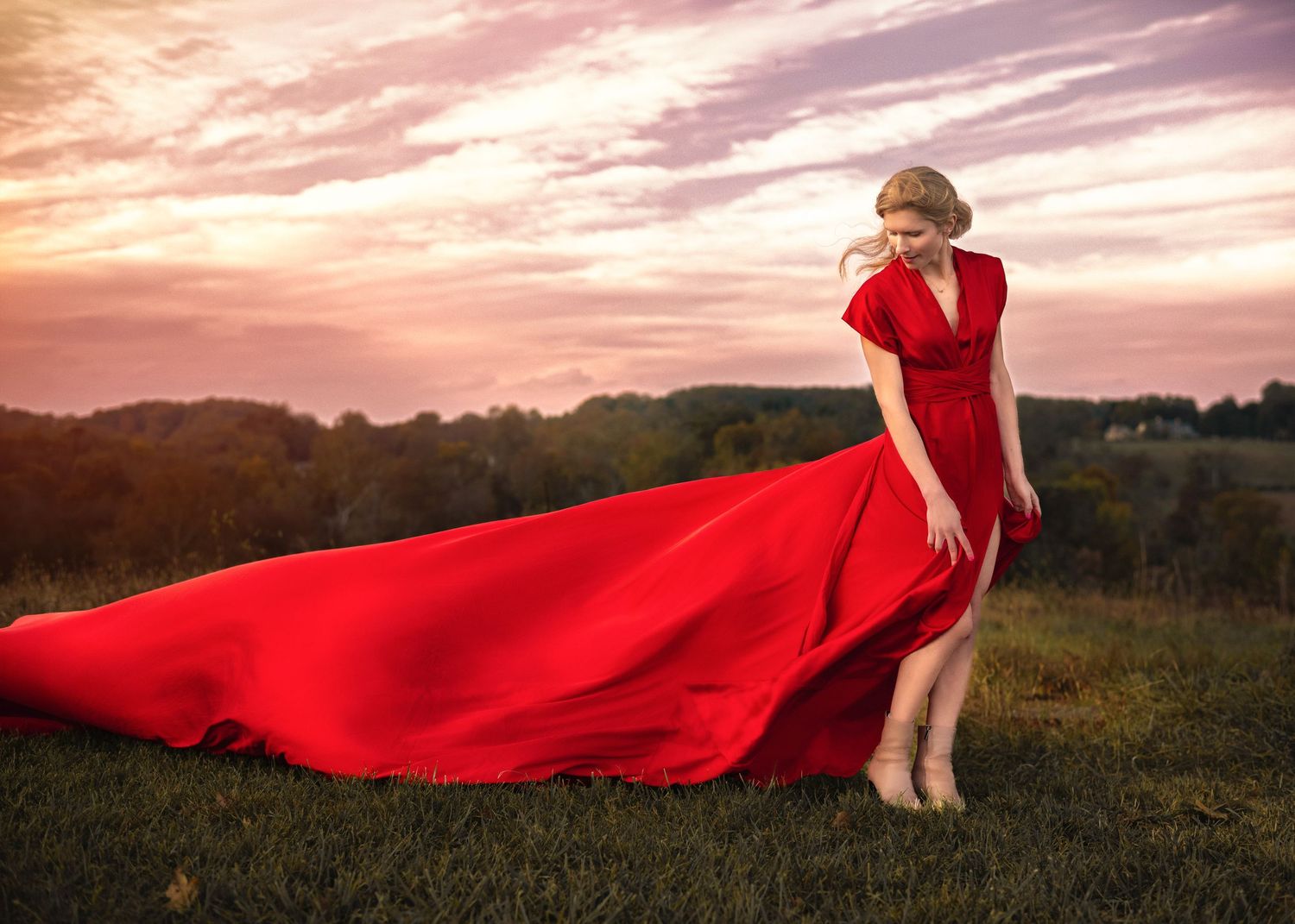 Woman in flowing red gown at sunset  dress billowing dramatically in the wind during her outdoor photography session on the Main Line, PA.