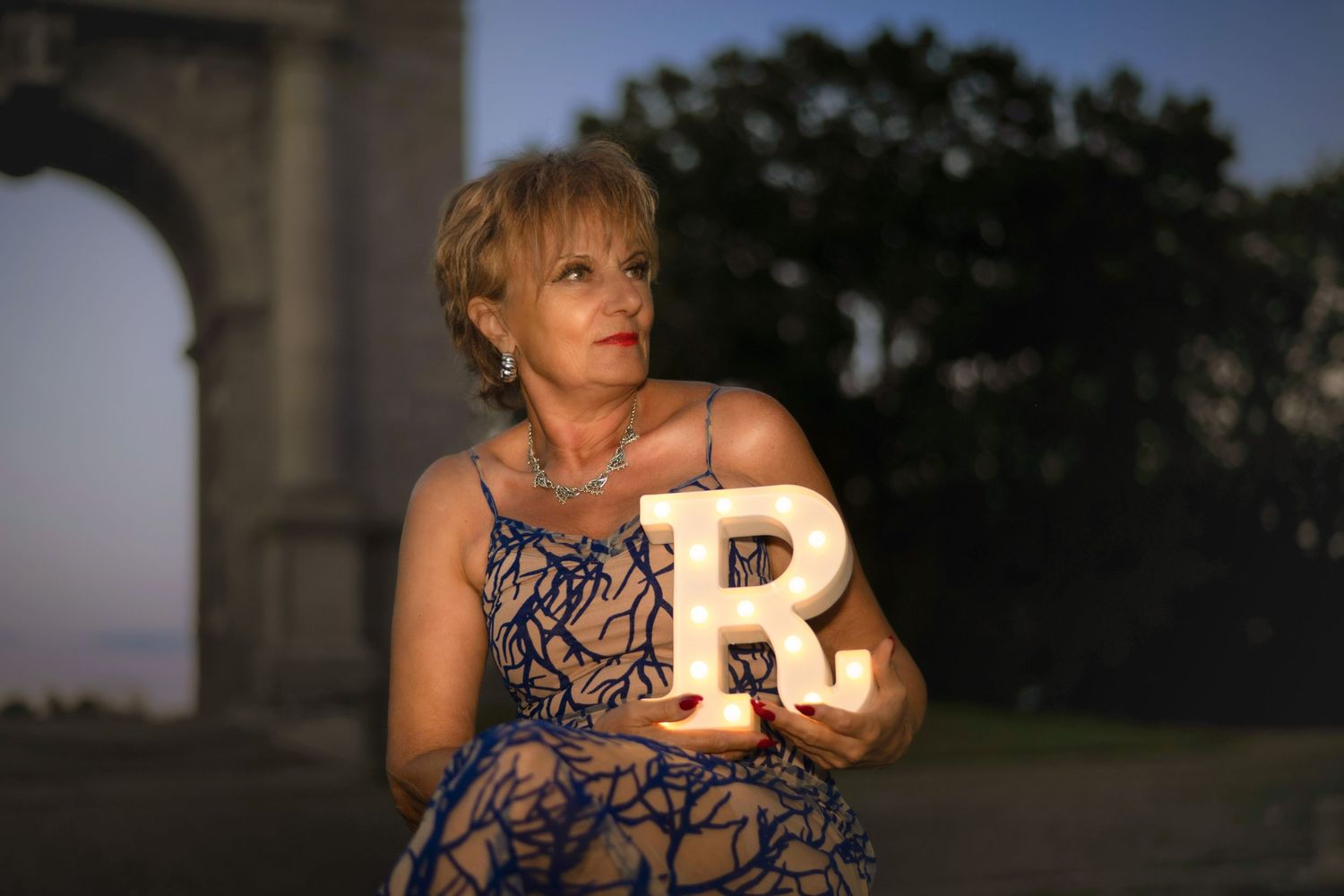 Person holding illuminated letter prop during twilight outdoor photoshoot.