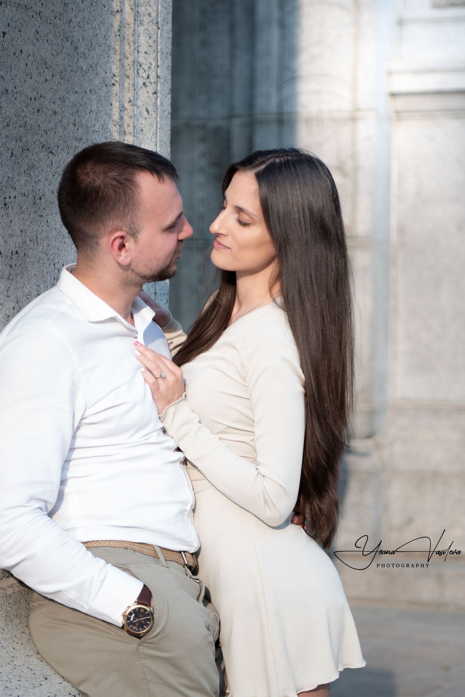 Romantic couple in white clothing sharing intimate moment against stone backdrop.