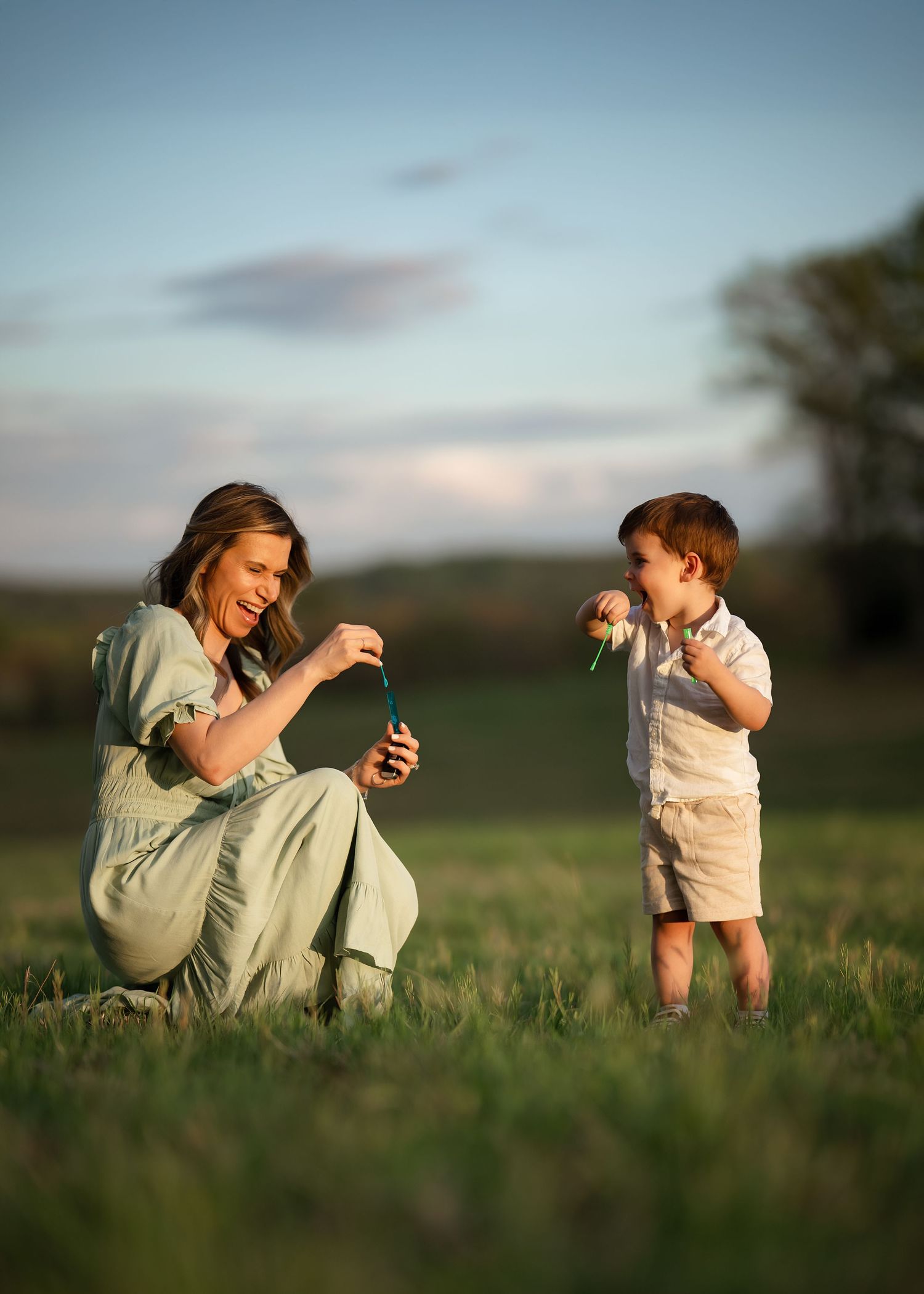 A mother and her young child sharing a playful moment blowing bubbles during their sunset golden hour Mommy & Me portrait session.