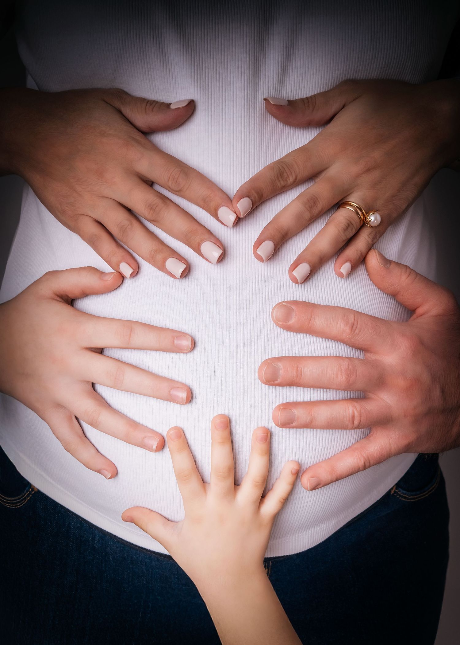 Pregnant woman's belly with three pairs of hands placed lovingly on it, symbolizing family and new life.