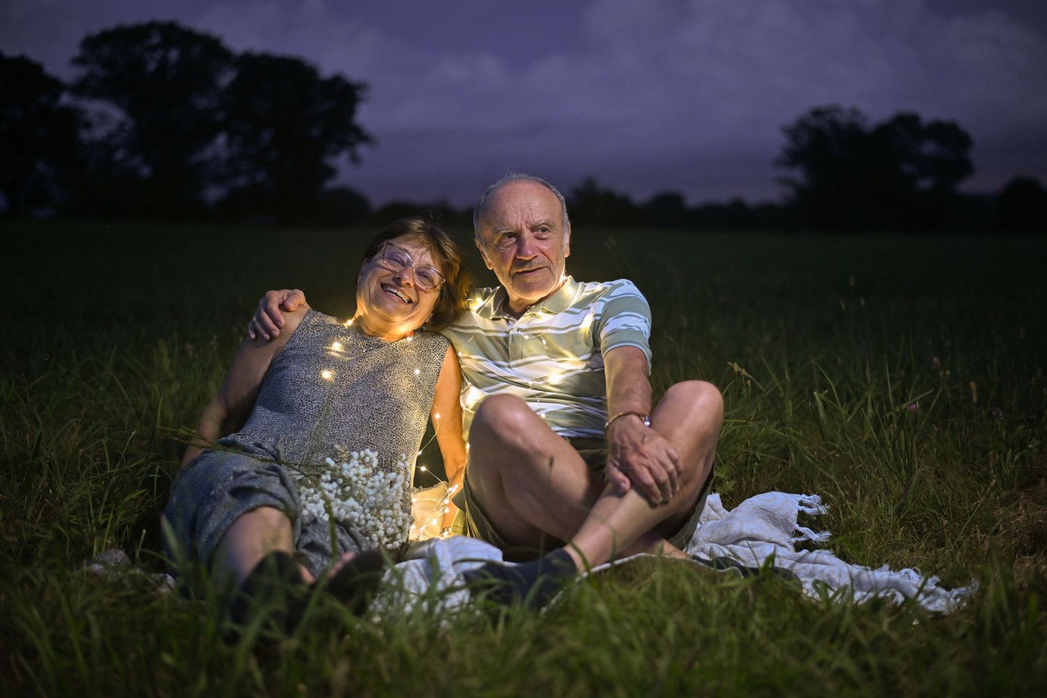 Romantic couple lying in a grassy field at sunset sharing an intimate moment.
