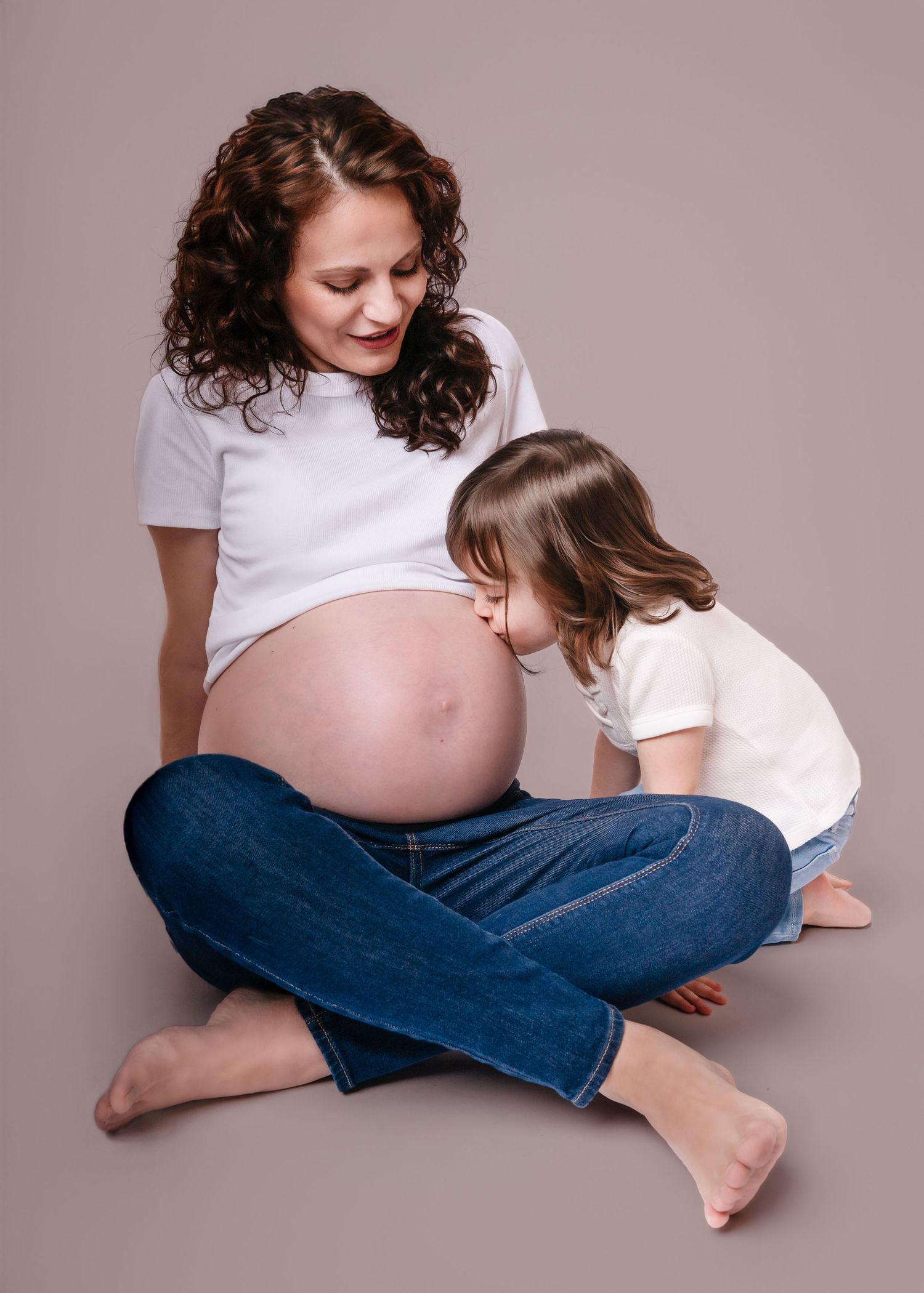 Young child kissing pregnant mothers bare belly during maternity photo session.