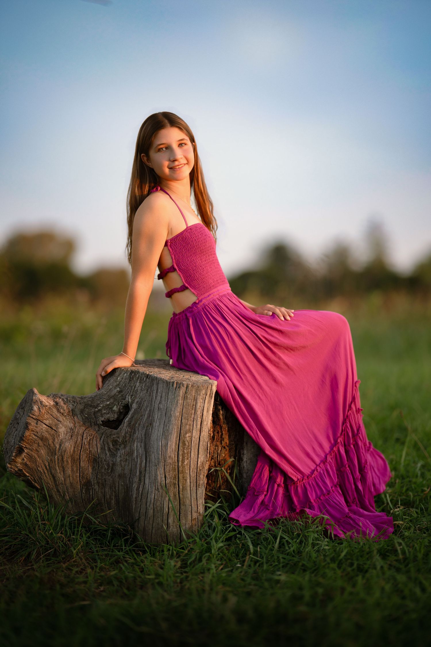 Senior girl in a pink dress seated by a tree during golden hour senior portrait session on the Main Line.