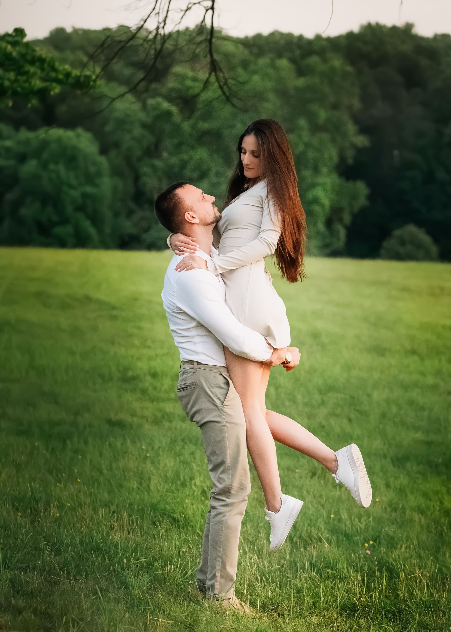 Engaged couple sharing a playful romantic moment in a lush green field on the Main Line.