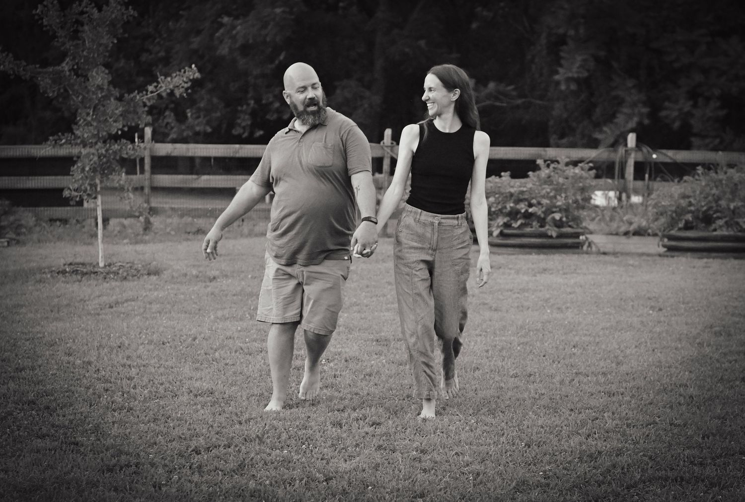Black and white photo captures couple walking together in a peaceful garden setting.