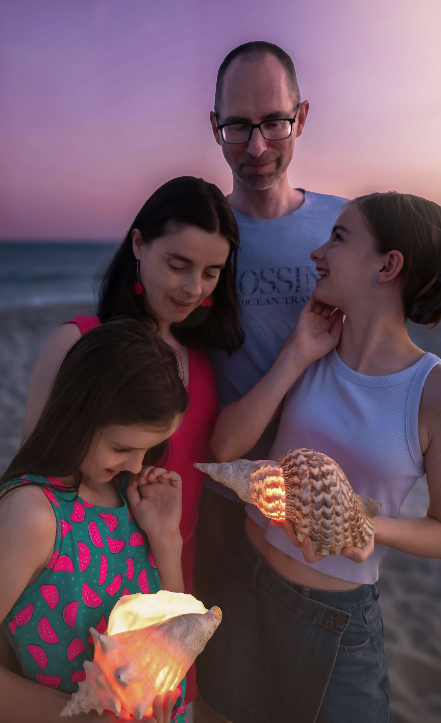 A family group on the beach at sunset holding illuminated seashells.