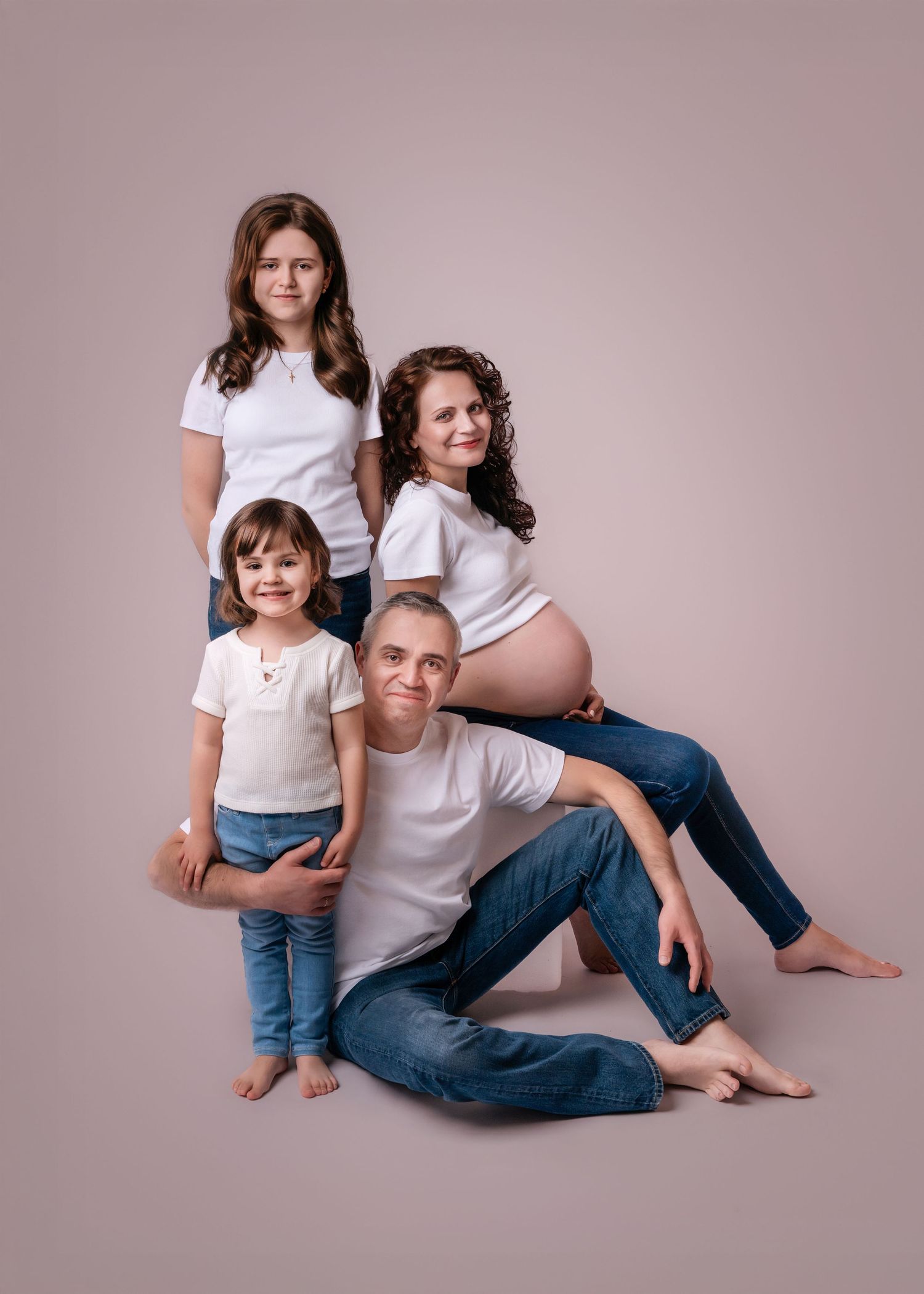 Family maternity photo with pregnant mother, father, and two children in white shirts and jeans.