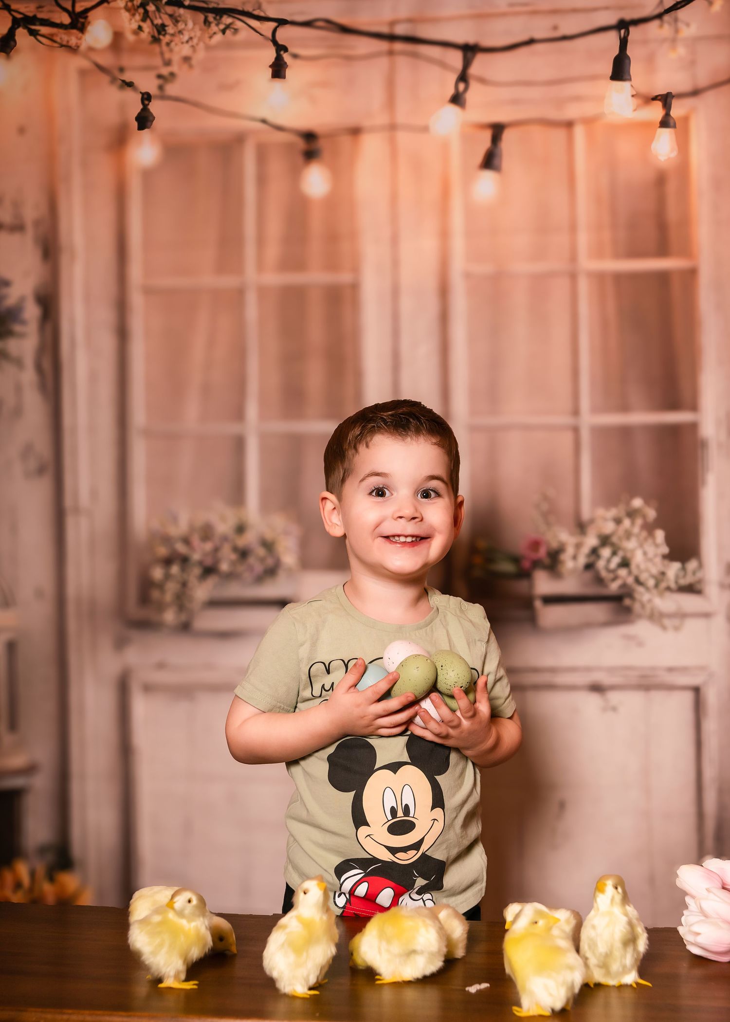 A smiling toddler holding Easter eggs near baby chicks during his holiday portrait session on the Main Line, PA.