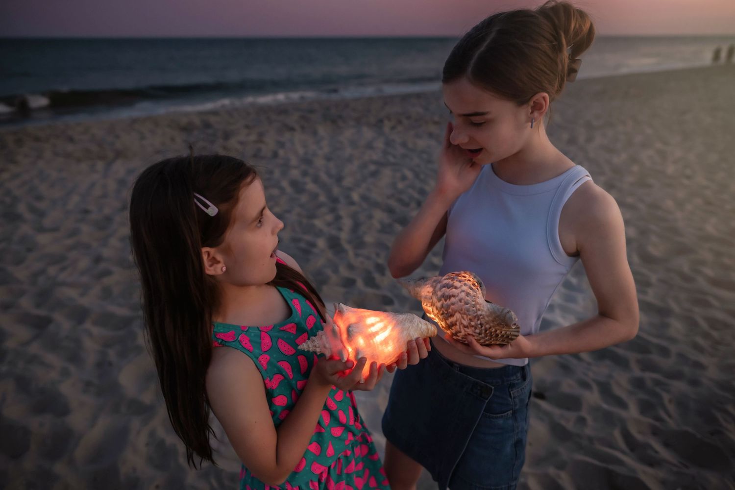 Two people sharing a moment with glowing seashells on a beach at dusk.