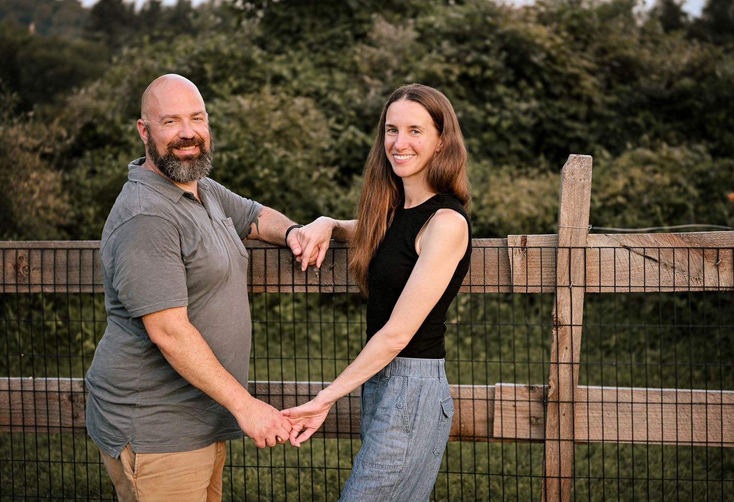 Couple poses affectionately in front of a wooden fence during golden hour.