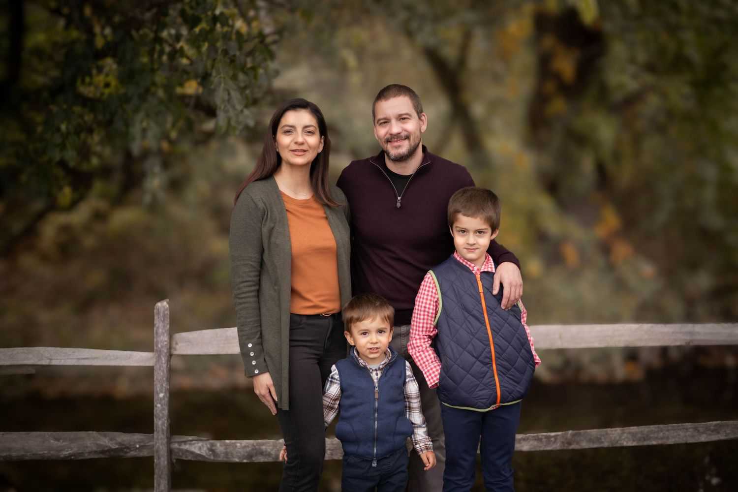 Family portrait session against rustic wooden fence during fall season.