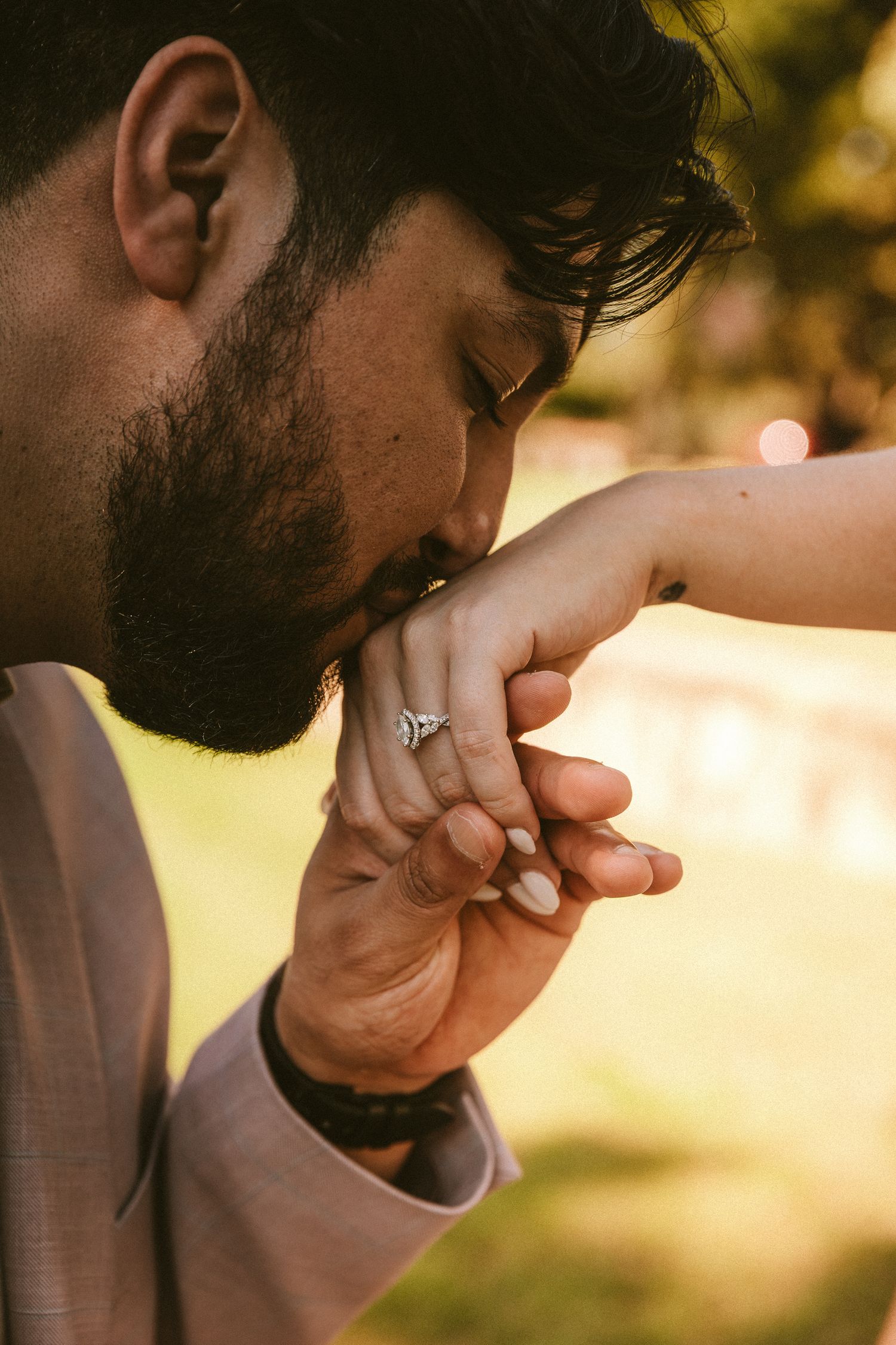 Close-up shot of a tender moment between two people holding hands in warm sunlight.