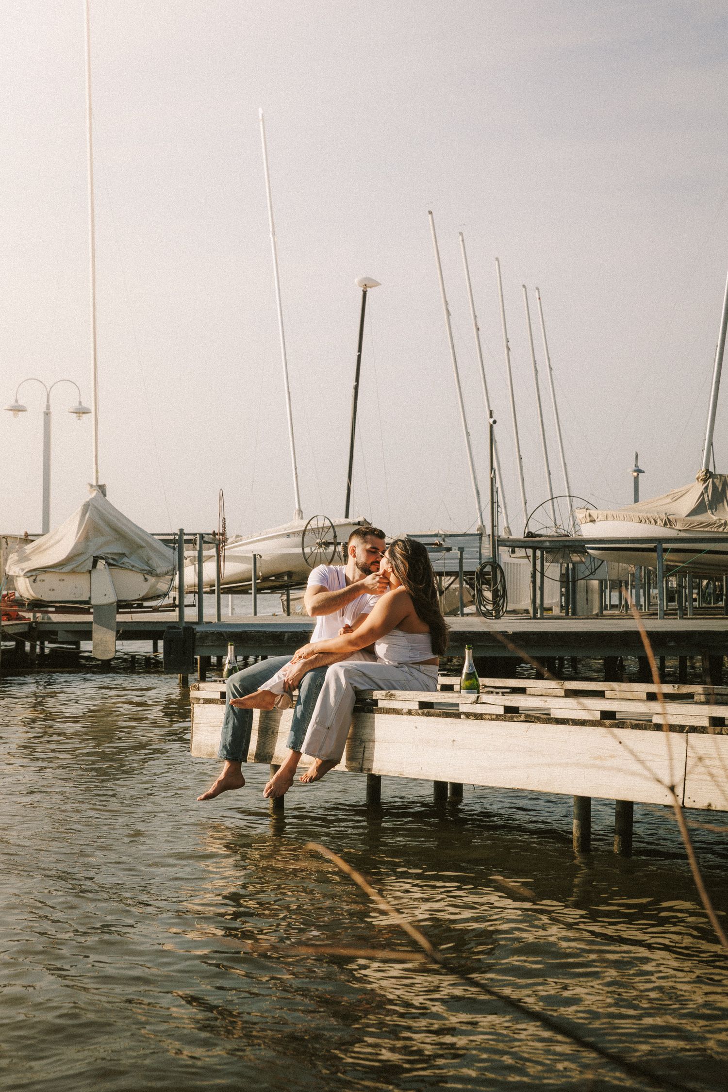 A couple sitting together on a wooden dock surrounded by boats at a marina.