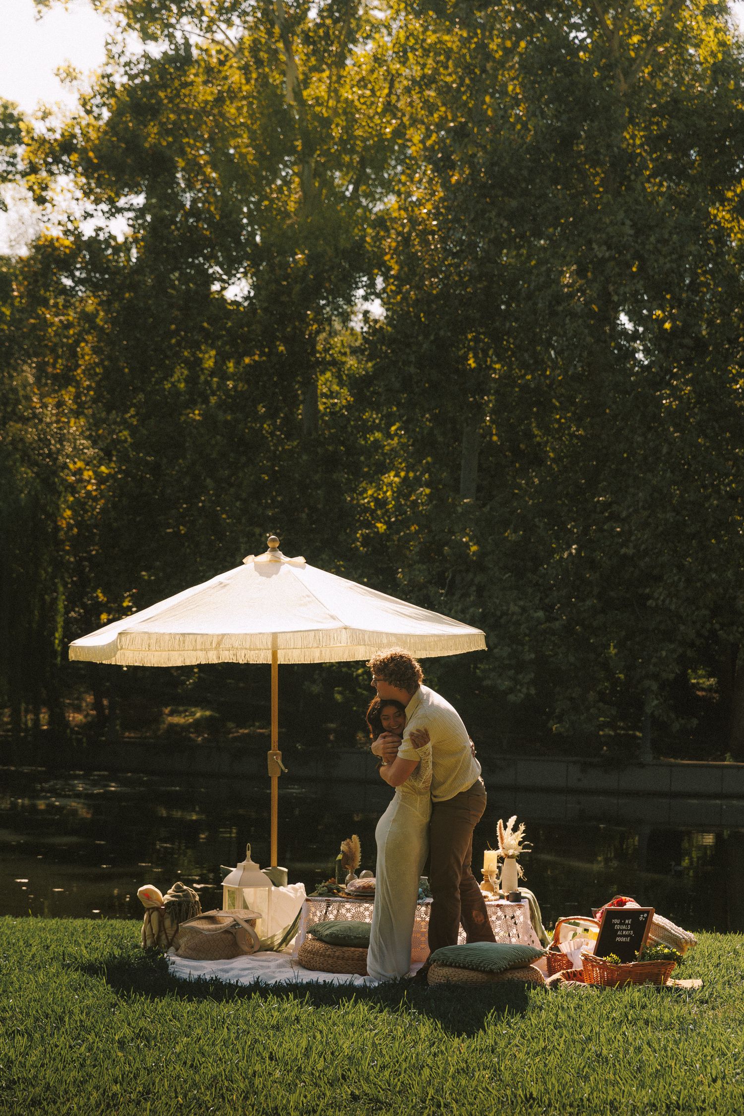 A romantic picnic setup in a park with a white umbrella and blankets during golden hour.