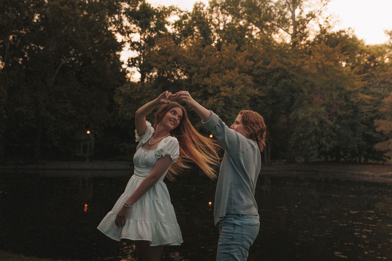 A couple dances together at sunset in a park with autumn trees in the background.