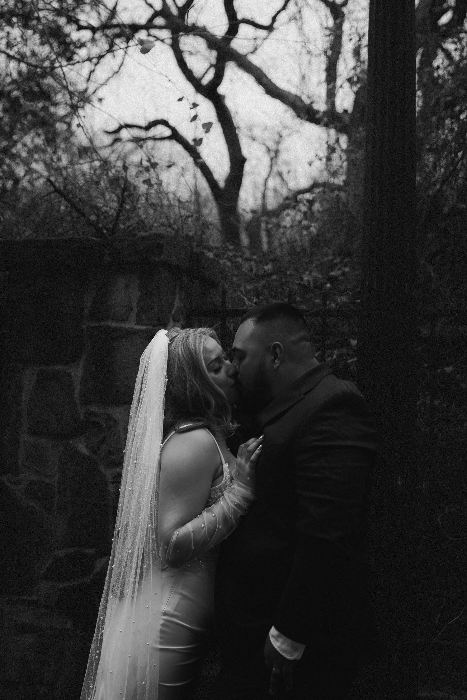 A romantic black and white wedding photo series showing a couple embracing in a wooded outdoor setting.