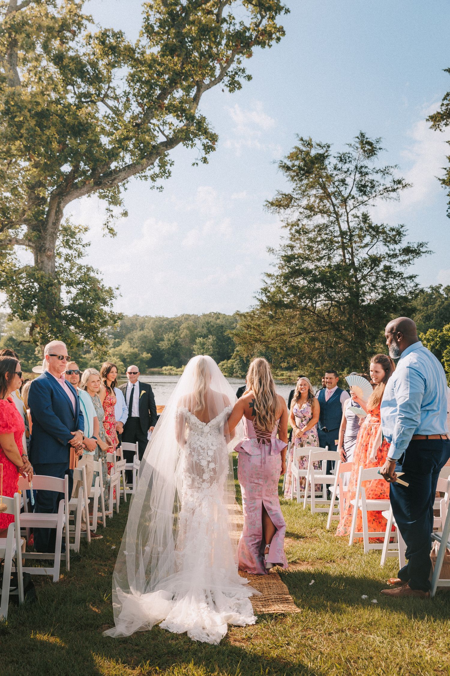 Wedding guests seated in white chairs for outdoor ceremony with scenic natural backdrop.