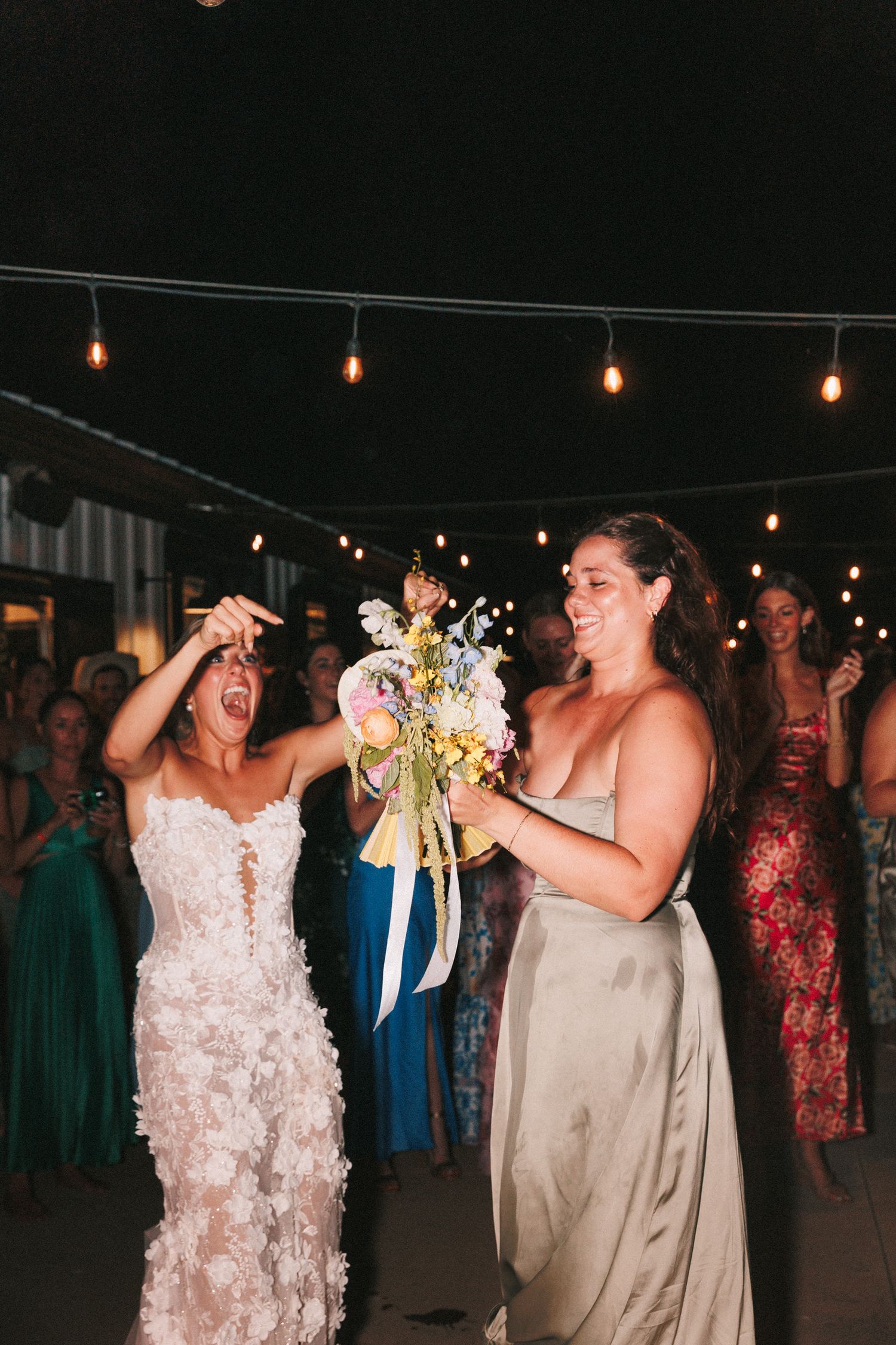Wedding party celebrating enthusiastically under string lights at night.