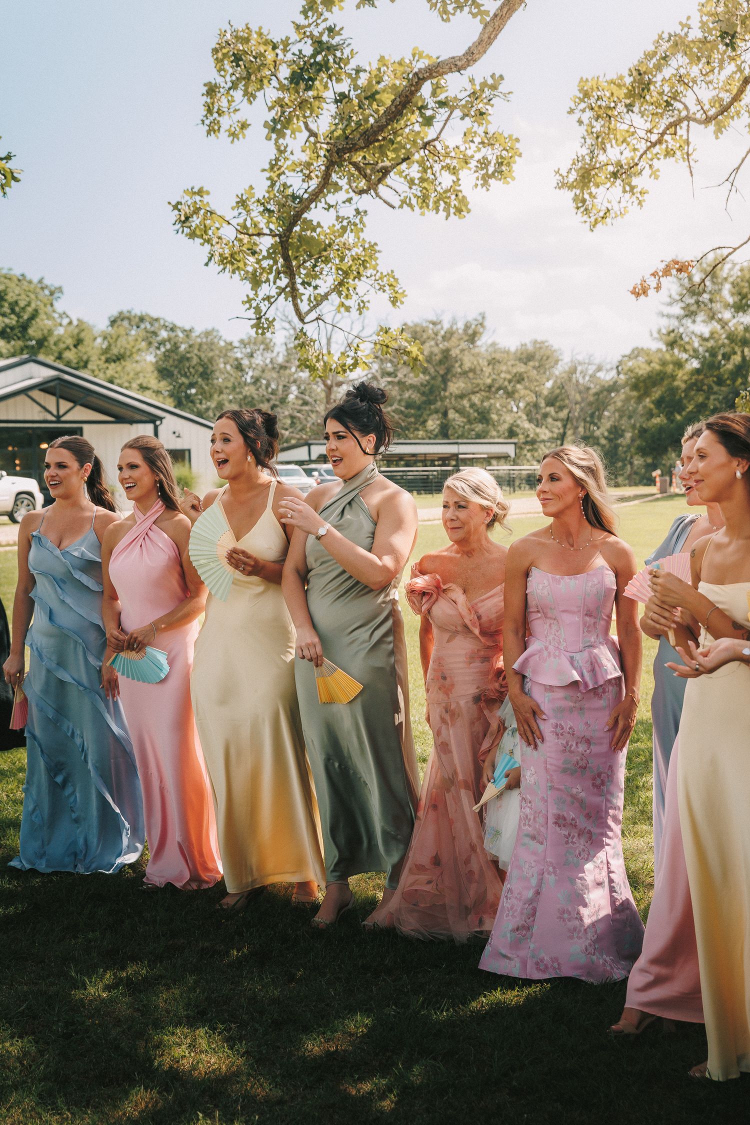 Row of bridesmaids wearing pastel-colored formal dresses standing together outdoors.
