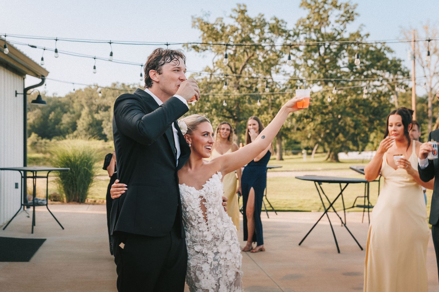 Wedding reception celebration with string lights and dancing outdoors at sunset.