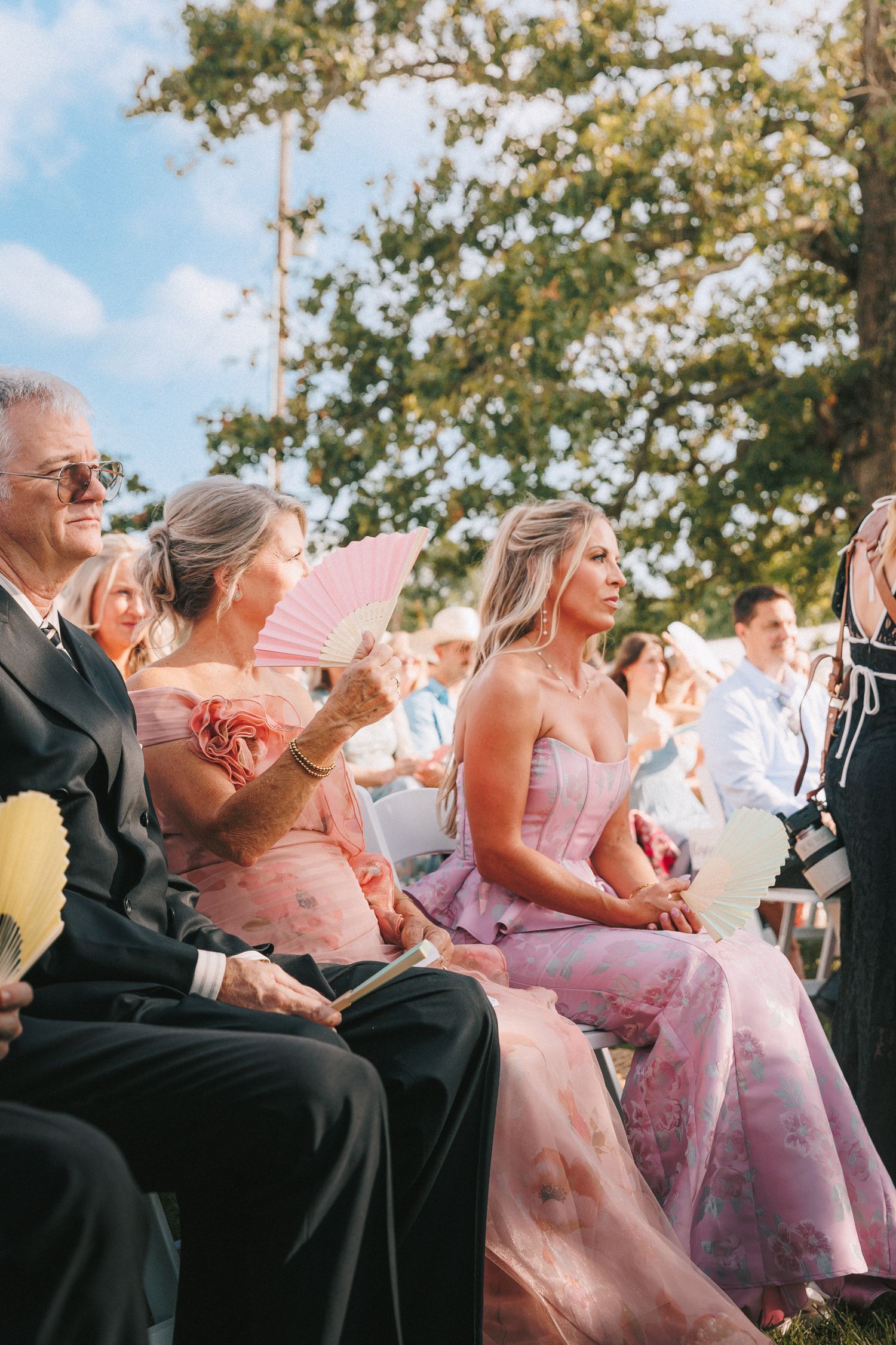 Wedding guests in formal attire seated outdoors during ceremony.