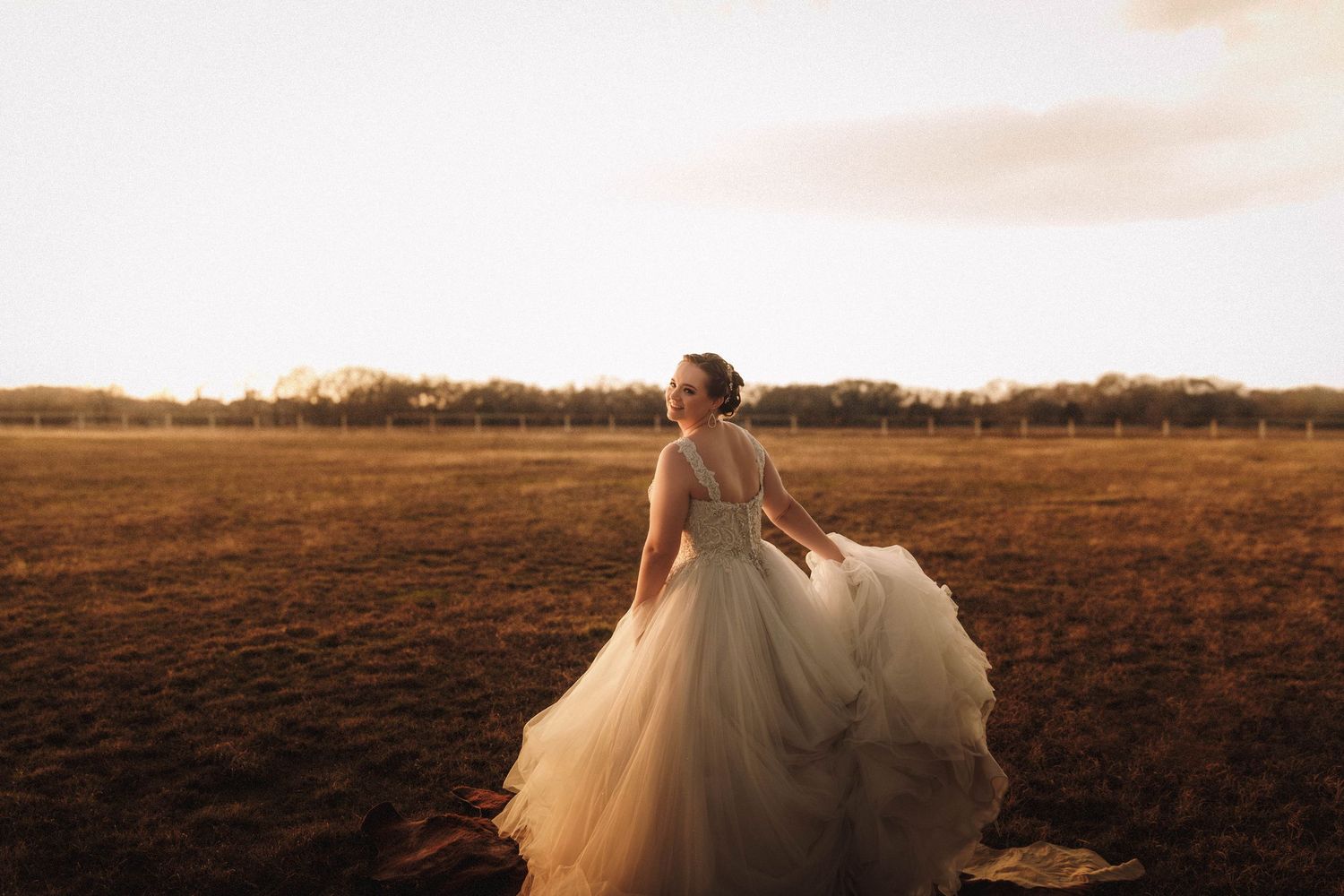 Golden sunset light illuminates a field with a flowing white dress in motion against a dramatic sky.