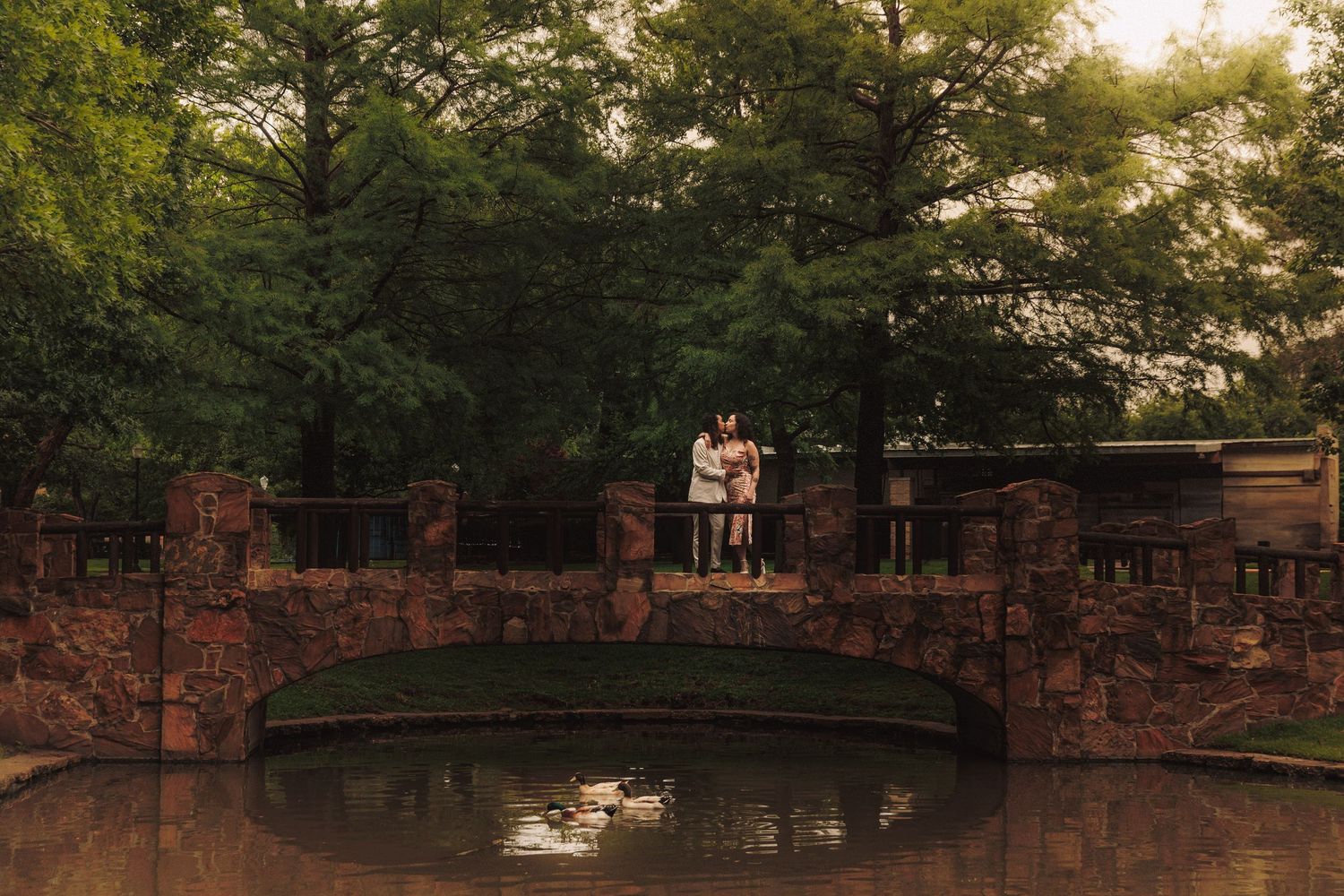 A couple shares a romantic sunset moment in a forest garden setting during an engagement photoshoot.