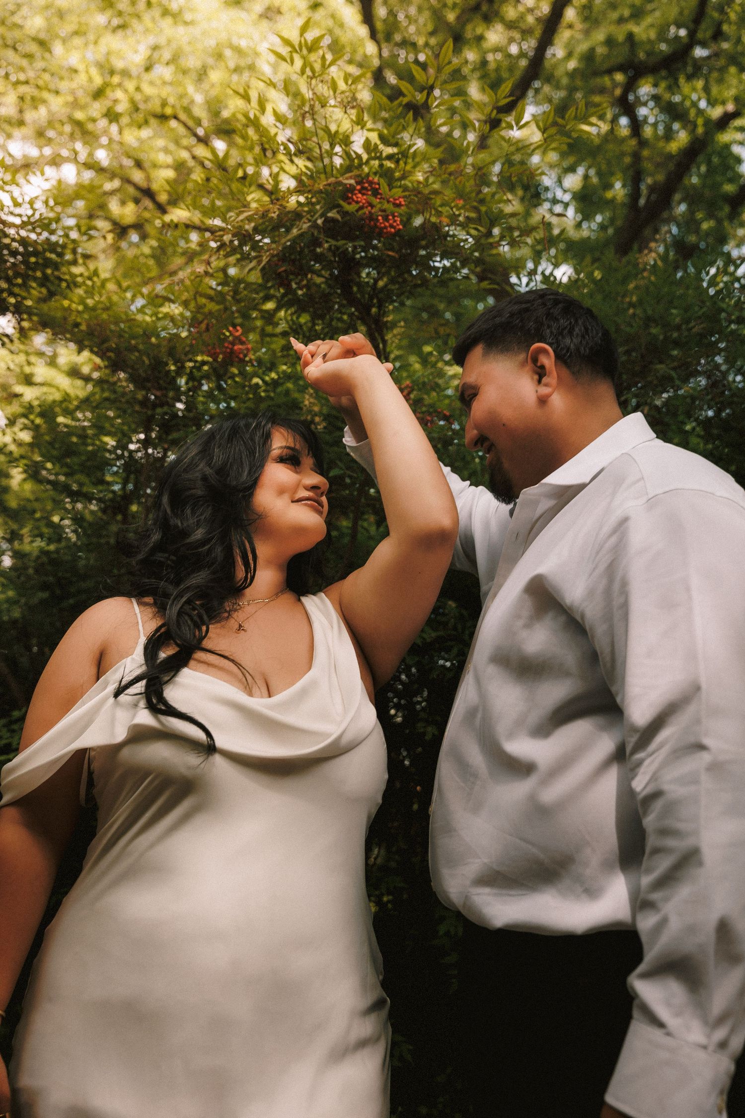 A couple shares an intimate outdoor photoshoot in natural lighting with lush greenery in the background.