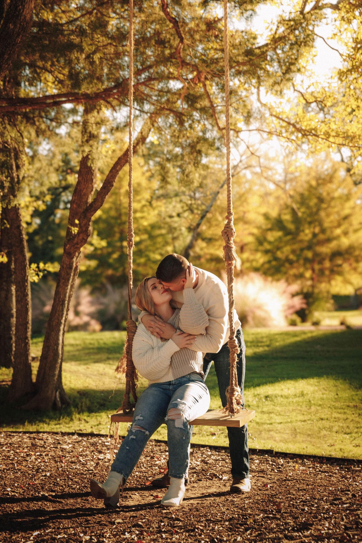 Couple shares intimate moments on fallen tree trunks in golden sunlit forest setting.
