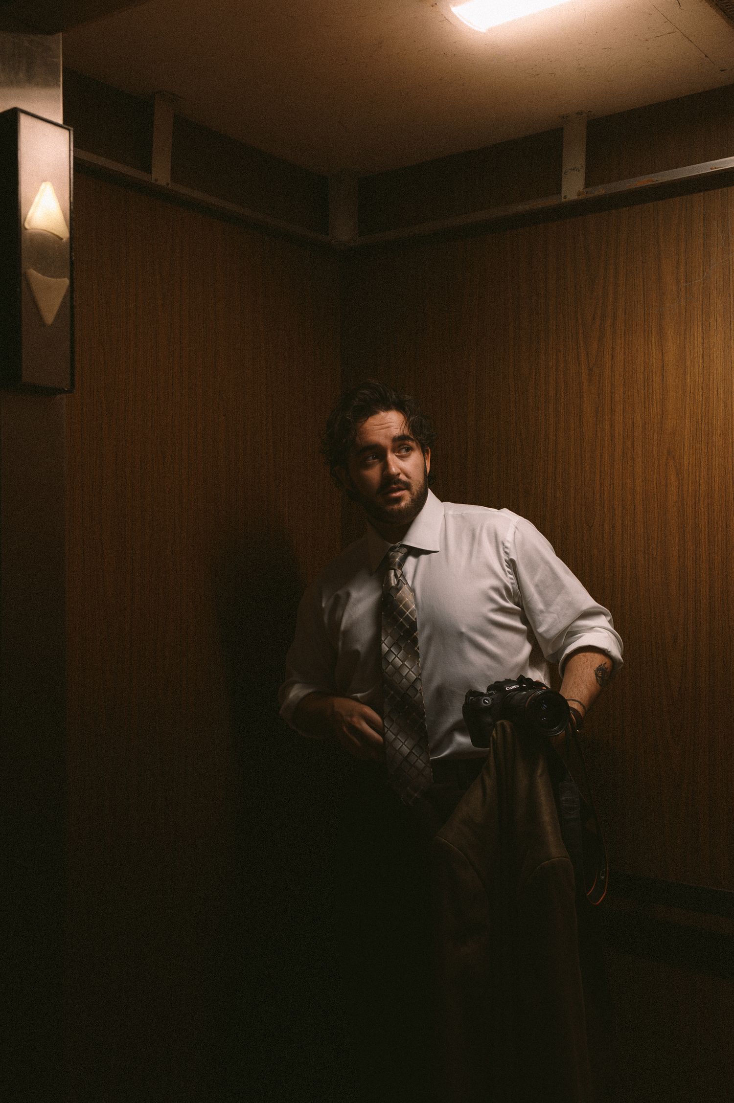 A dark moody sequence of someone in a white shirt moving through a dimly lit wood-paneled room.