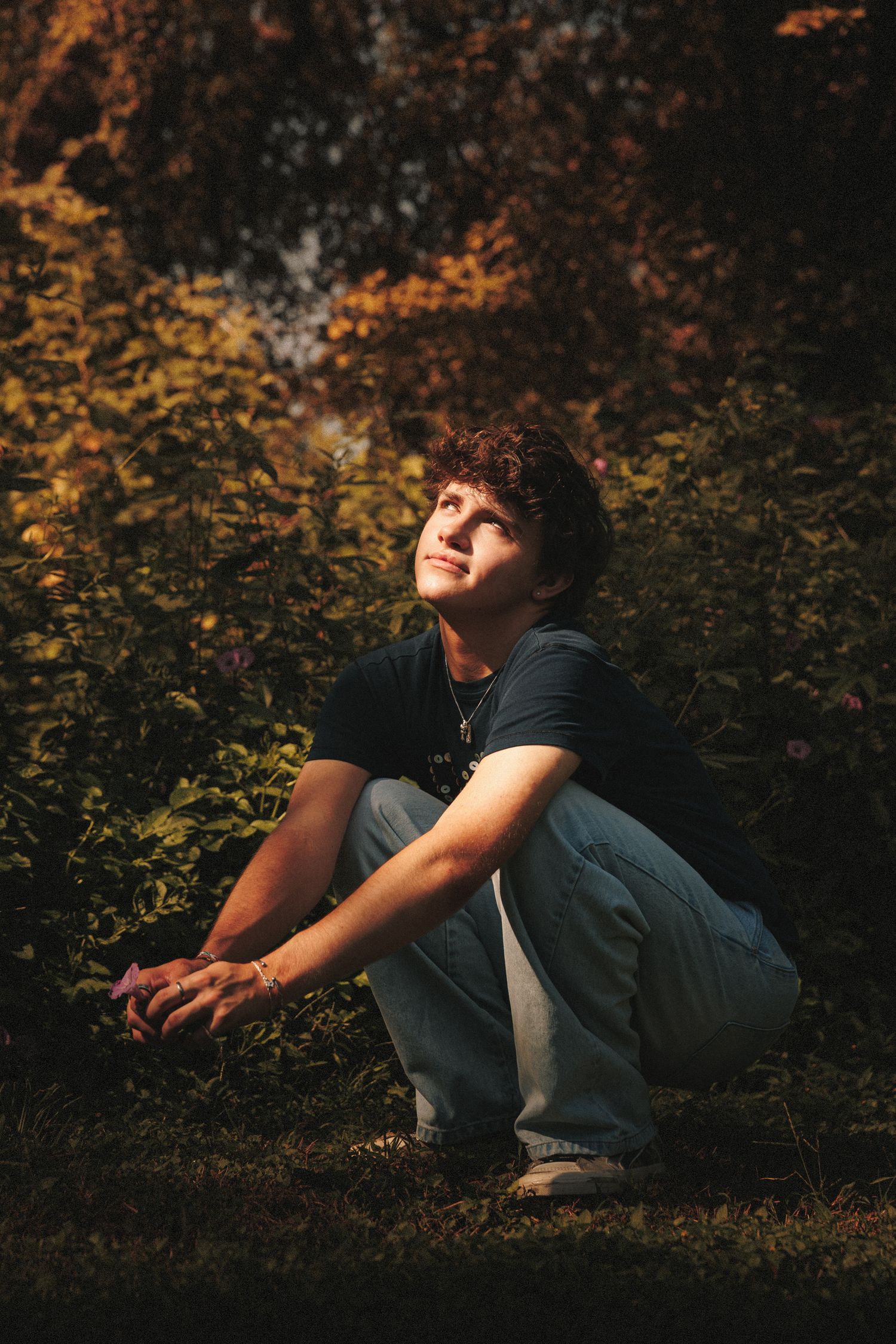 Person lying on grass in autumn setting with golden leaves and moody lighting creates dreamy outdoor portrait.