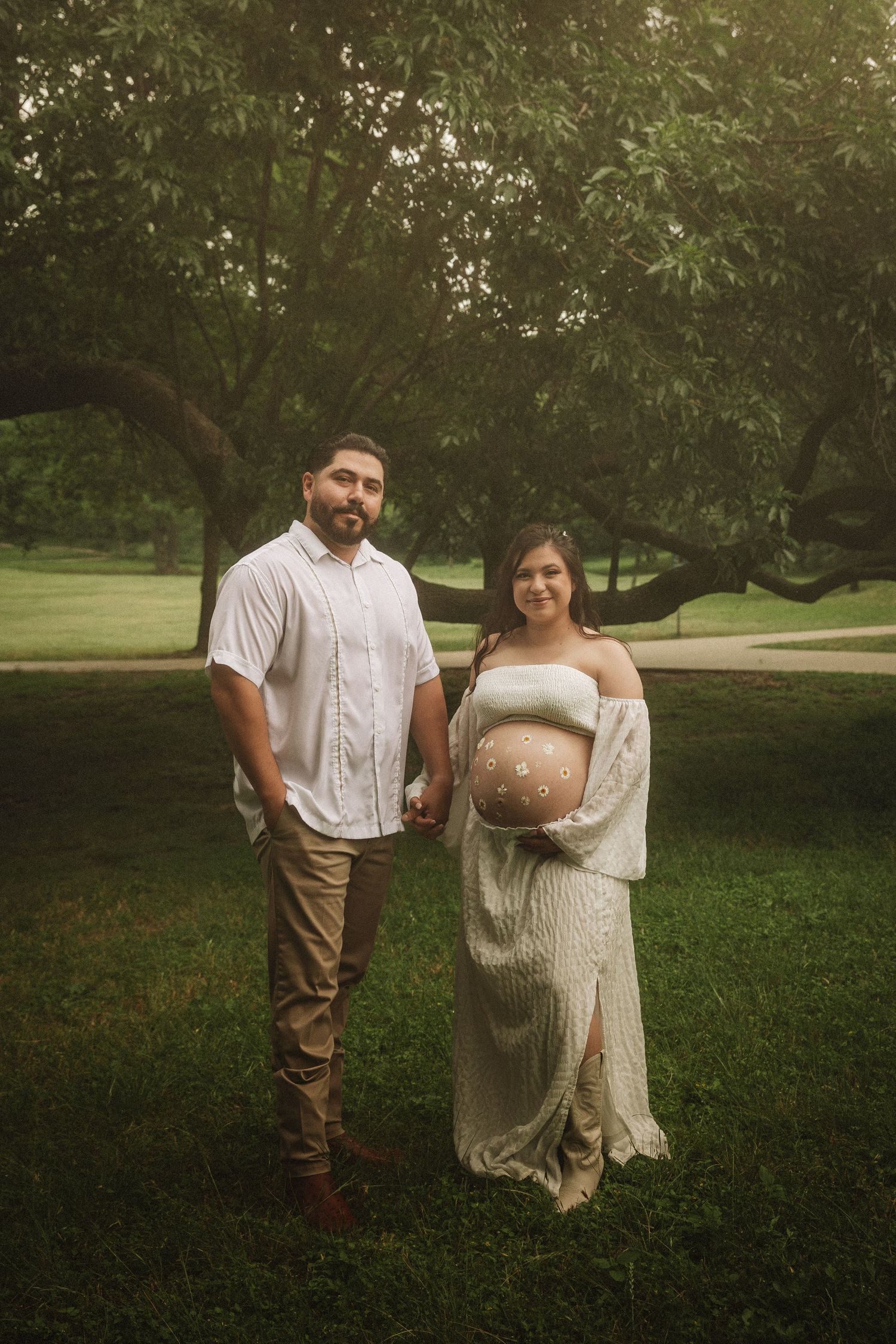 A couple poses together in a romantic outdoor setting with green grass and trees in the background.
