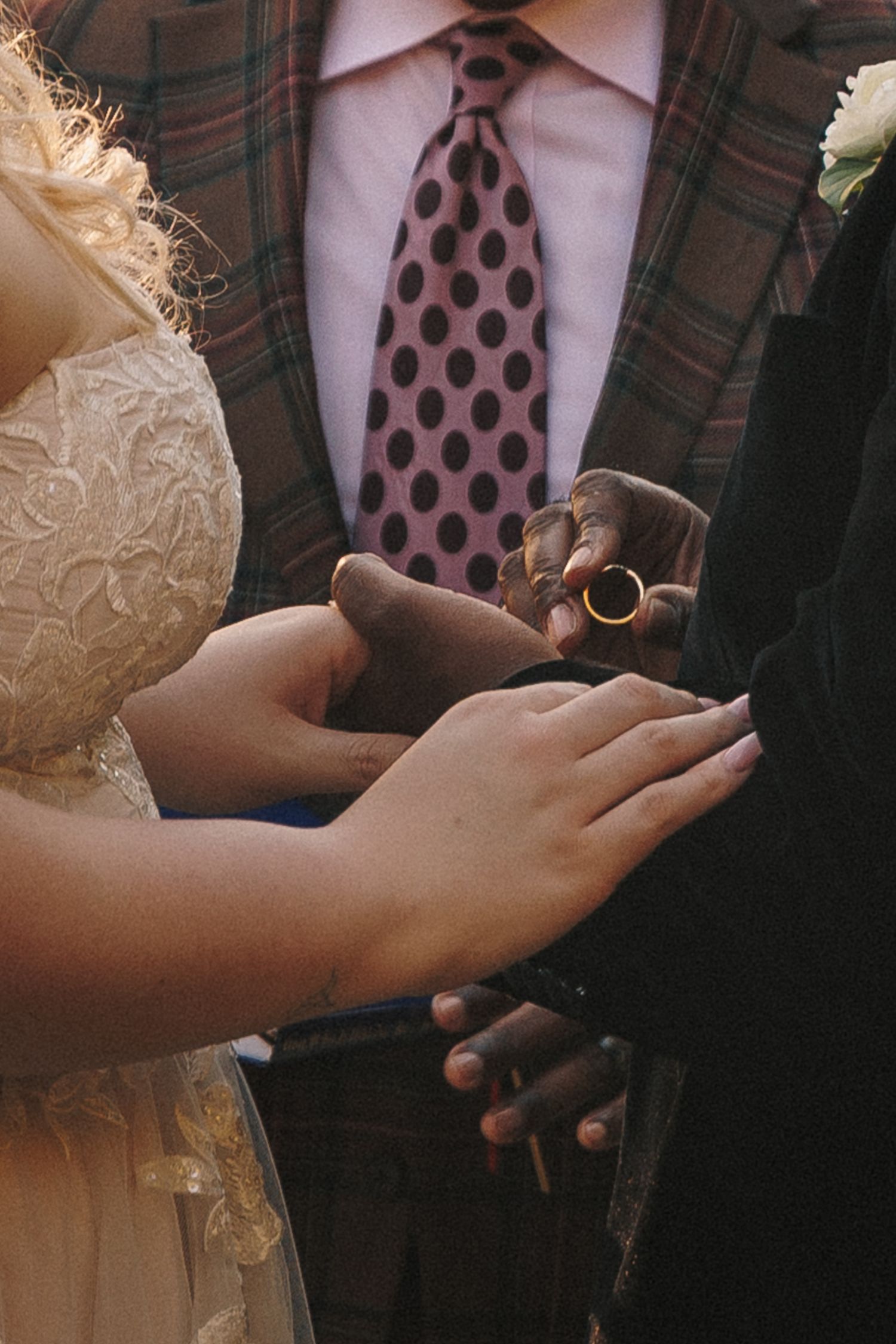 Close-up of wedding rings being exchanged, groom wearing plaid jacket and polka dot tie.