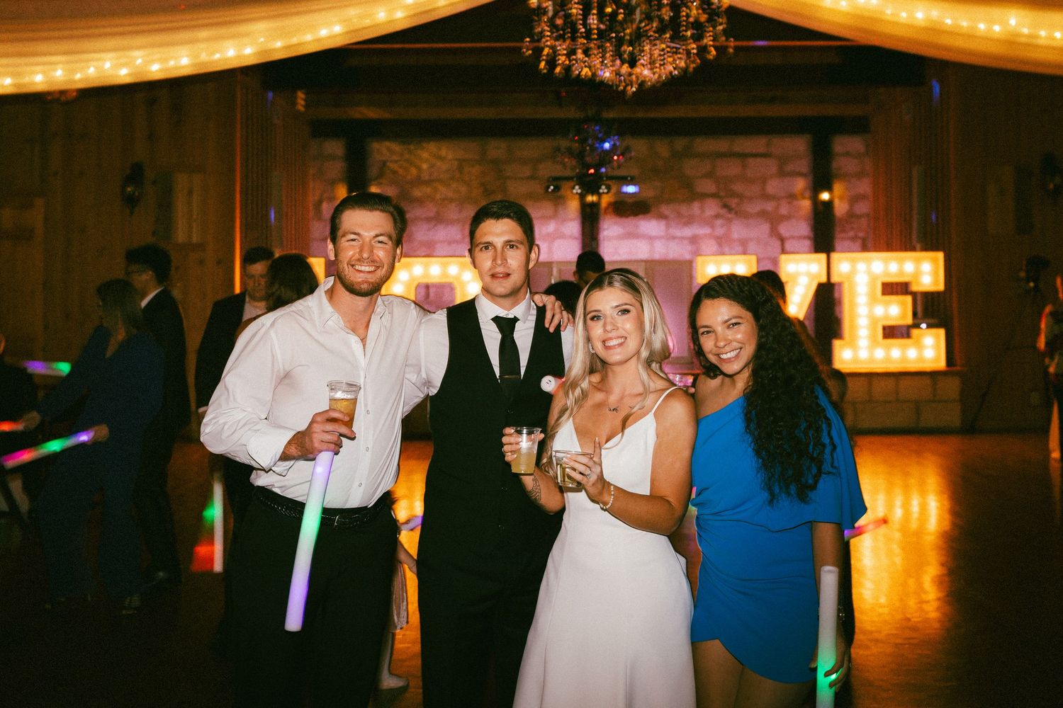 Bride and groom pose with two guests on the dance floor at wedding reception.