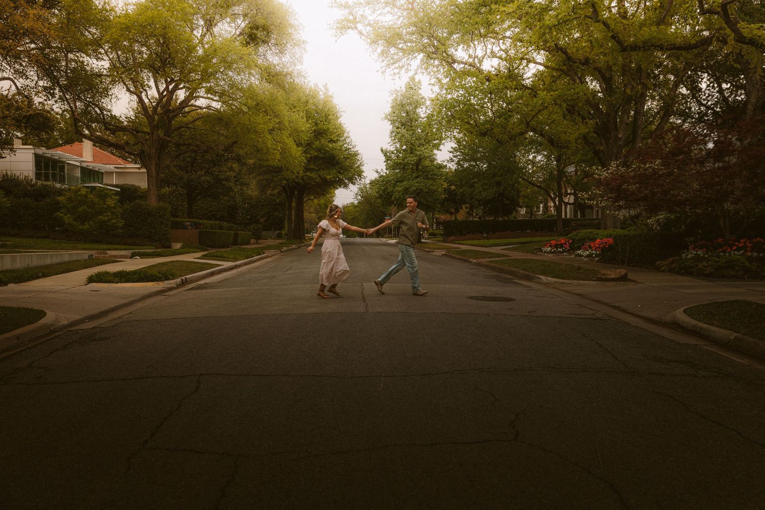 Couple holding hands and dancing in the middle of a tree-lined residential street.