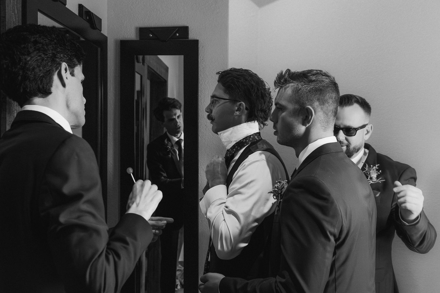 Black and white photo of groomsmen helping each other get dressed before a wedding ceremony.