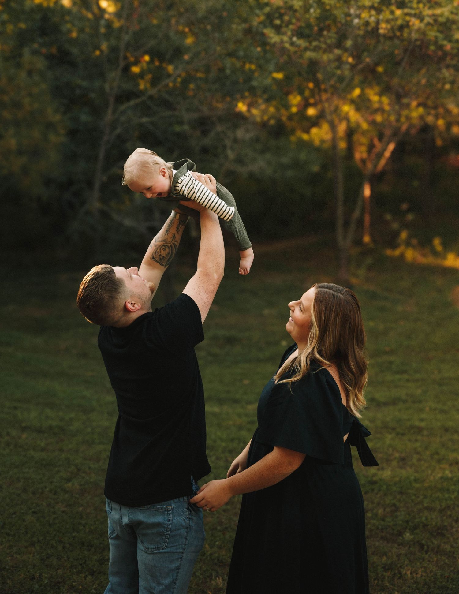 Couple playfully shares a drink from a glass bottle in a sunlit autumn field during golden hour.
