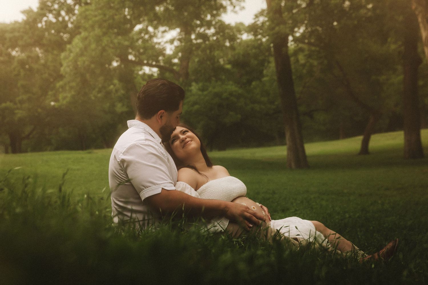 Couple sharing loving embrace on grass in park during golden sunset.