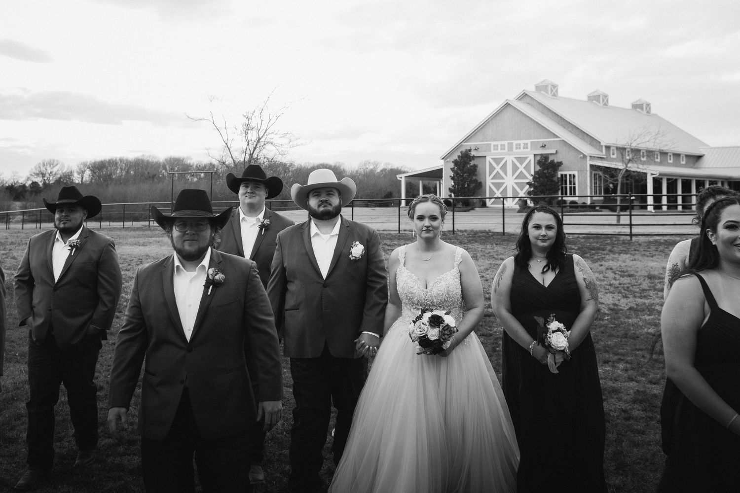 Wedding party stands in line outdoors with a rustic farmhouse and fields in the background.