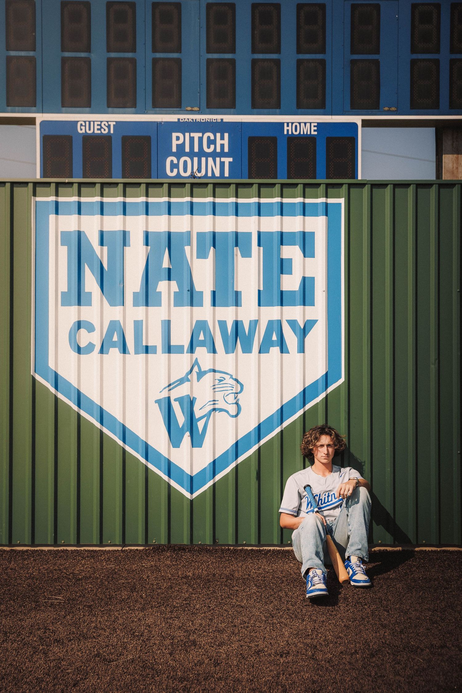 Baseball dugout wall with blue and white home plate shaped signs showing 'Callaway' branding at a sports facility.