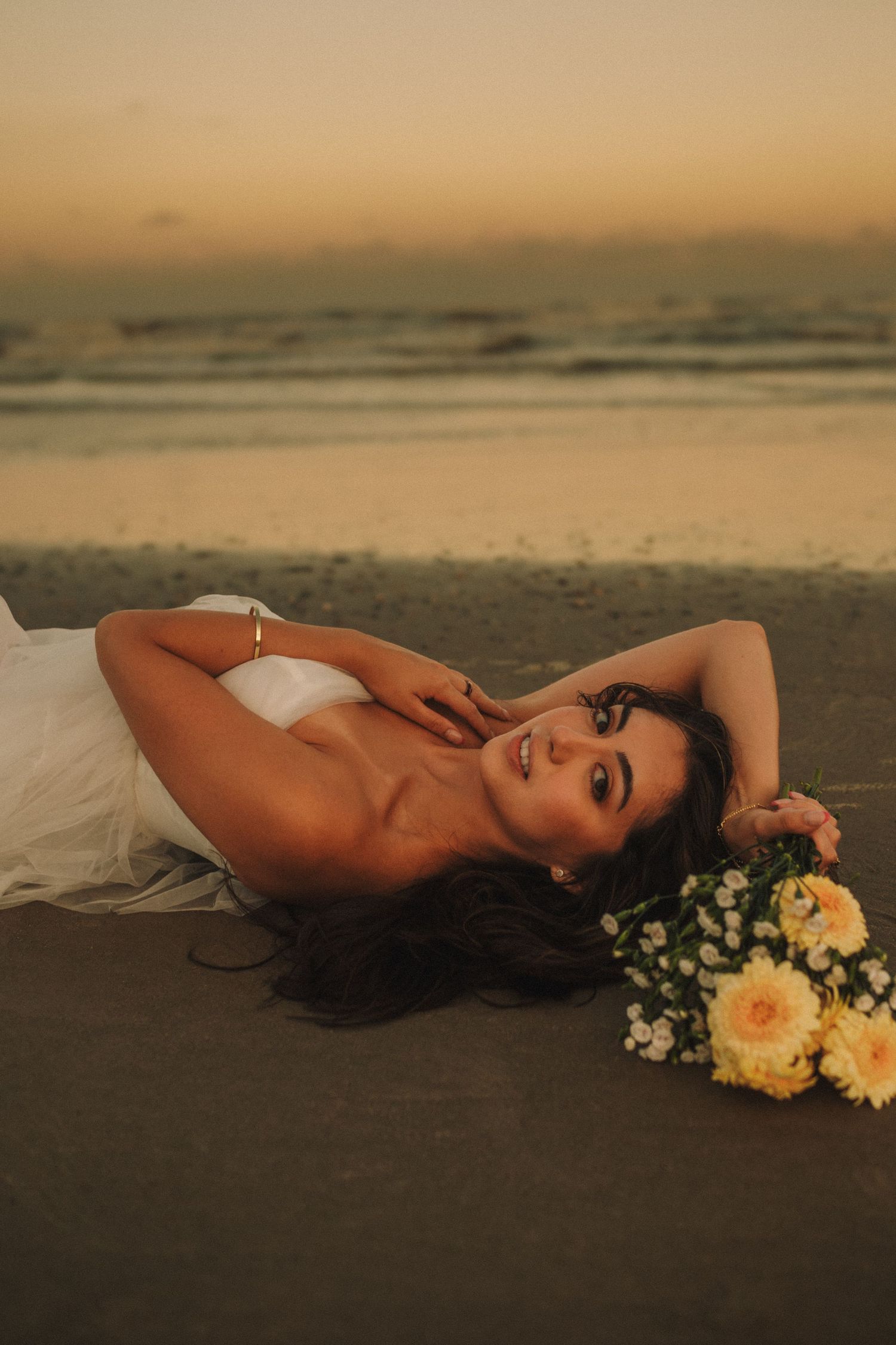 A romantic sunset beach photoshoot featuring elegant poses with peach and white floral bouquets on sandy shore.