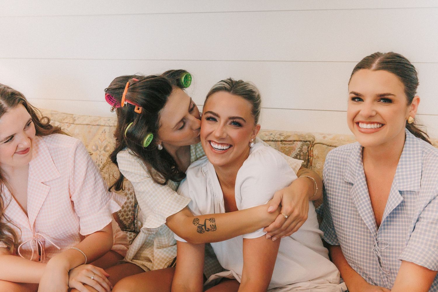 Wedding party members smile and embrace while getting ready in a bright indoor setting.