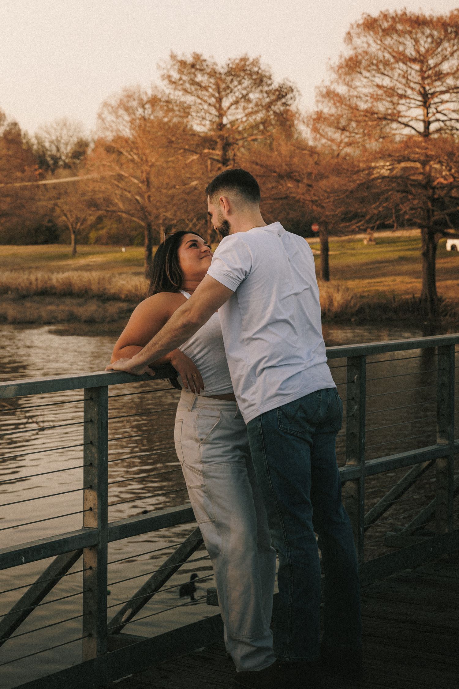 A couple shares an intimate moment along a waterfront railing at sunset.