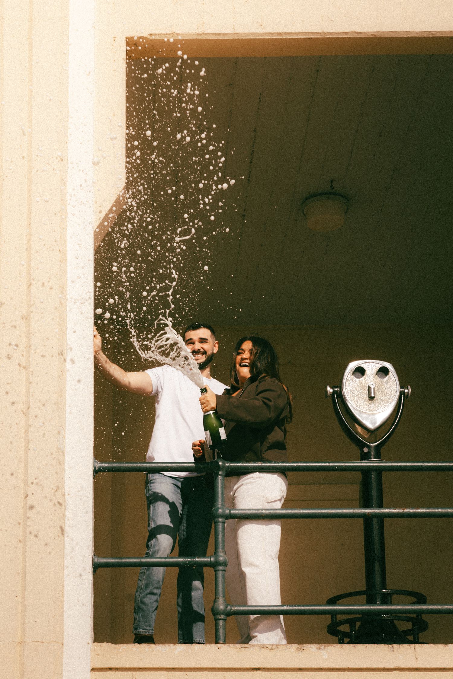 A couple embraces on a balcony overlooking the water at sunset with a Halloween pumpkin decoration nearby.