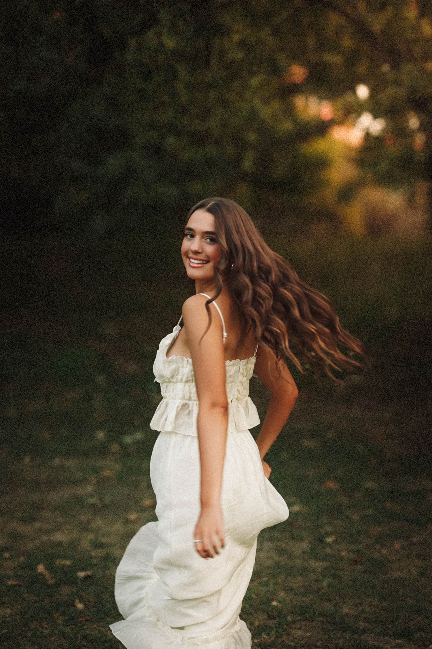 A person in a flowing white dress twirls joyfully in a sunlit outdoor setting during golden hour.