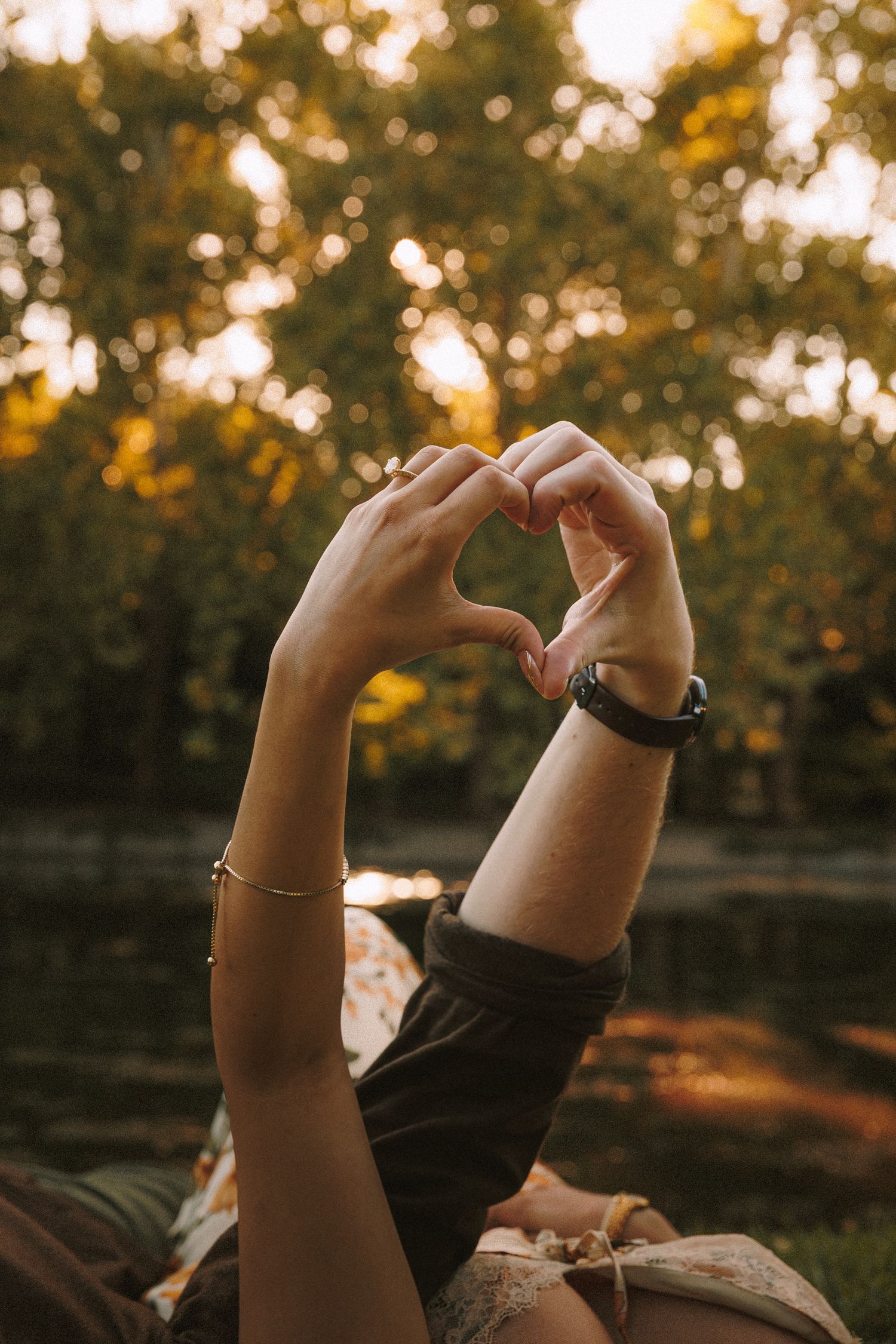 A person's hands raised against a warm sunset backdrop with golden bokeh through autumn trees.