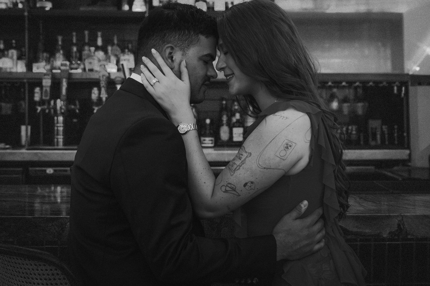 Black and white photo of a couple sharing a romantic moment at a bar, embracing and about to kiss.