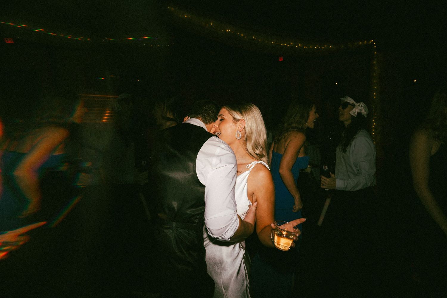 Bride in white dress dancing and celebrating with guests on crowded wedding reception dance floor.