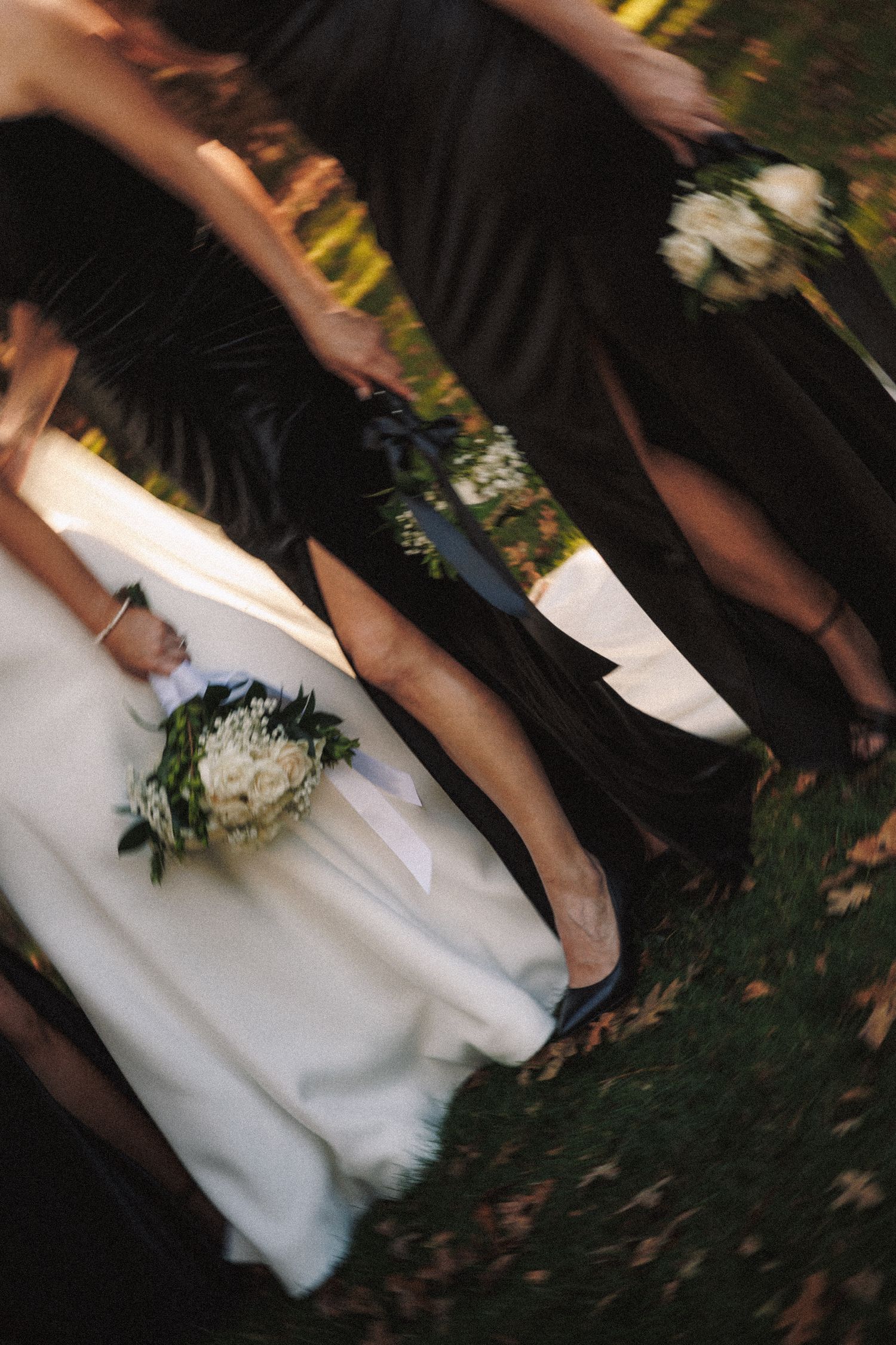 Bride in white gown walking with bridesmaids in black dresses carrying white floral bouquets.